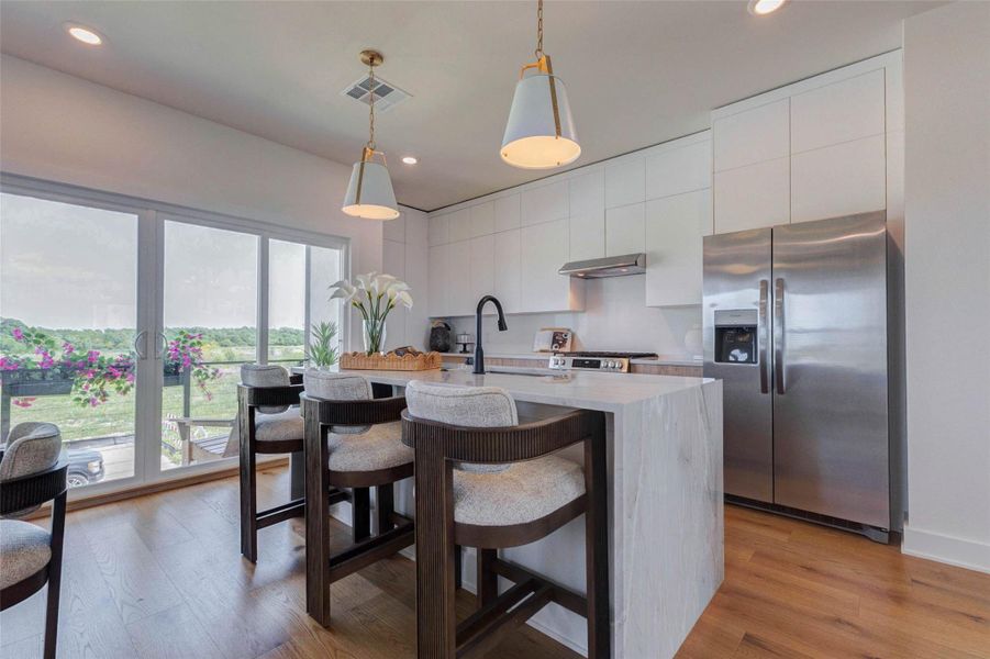 This polished kitchen pairs clean-lined cabinetry with warm wood accents, stainless-steel appliances, and a dramatic waterfall-edge island. Three counter-height seats make the island perfect for casual dining, conversation, or morning coffee, while oversized sliding doors invite abundant natural light and outdoor views. Stylish pendant lighting and a matte-black faucet complete the fresh, contemporary design.