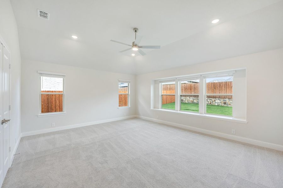 Empty bedroom with light carpet, ceiling fan, and multiple windows overlooking a backyard Empty bedroom with light carpet, ceiling fan, and multiple windows overlooking a backyard