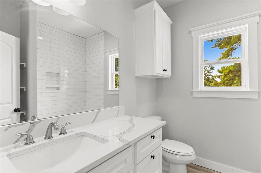 This bathroom features a clean, modern design with white subway tiles in the shower area, a double vanity with beautiful white quartz countertop. There's ample storage with a tall cabinet and under-sink drawers.