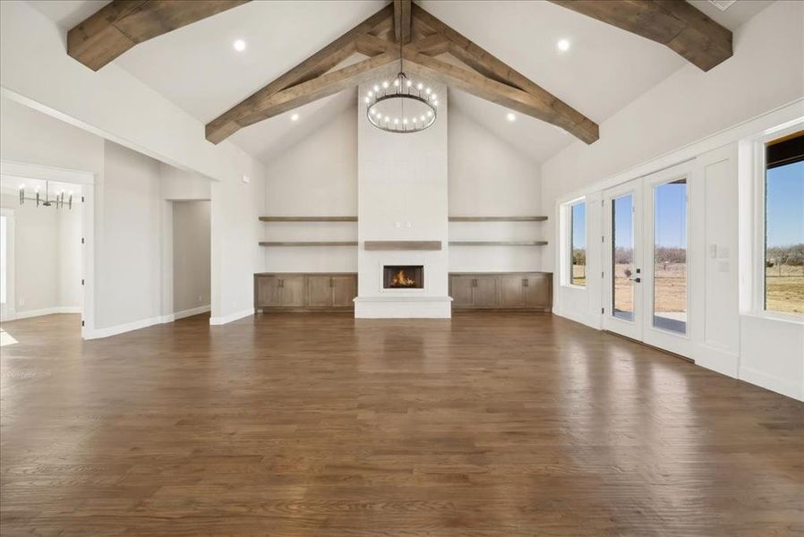 Unfurnished living room with an inviting chandelier, high vaulted ceiling, a fireplace, dark hardwood / wood-style flooring, and beamed ceiling