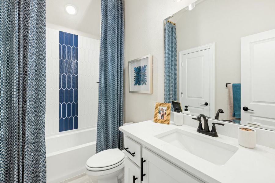 Bathroom with white vanity, tub-shower combo with blue tile accent, and patterned curtain Bathroom with white vanity, tub-shower combo with blue tile accent, and patterned curtain