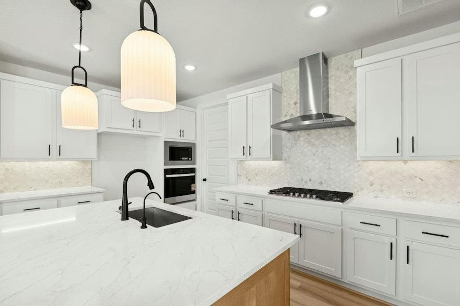 Kitchen with hanging light fixtures, tasteful backsplash, light stone countertops, white cabinets, and light wood finished floors