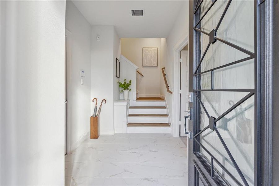 This stylish entryway sets the tone for this 3-bedroom, 3.5-bathroom home. Sleek tile floors and an open staircase lead up to the main living areas, while a custom-designed front door adds a touch of sophistication. To the right of the entry is a first floor bedroom with ensuite bathroom.