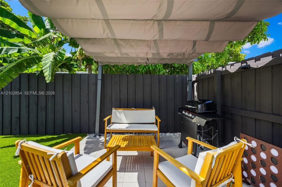 Outdoor patio featuring light-toned concrete pavers, a retractable overhead canopy, and a dark-toned privacy fence