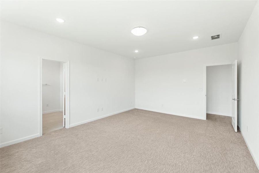 Empty bedroom with beige carpet, white walls, recessed lighting, and two open doorways leading to closet and hallway