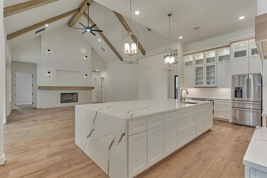 Stunning view from the kitchen showcasing the expansive waterfall island, custom cabinetry, stainless steel appliances, and vaulted living room with a modern shiplap fireplace.