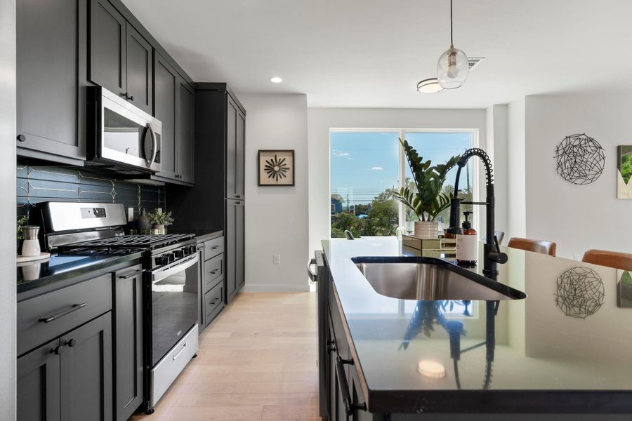 Kitchen featuring appliances with stainless steel finishes, pendant lighting, light wood-style floors, tasteful backsplash, and dark cabinets