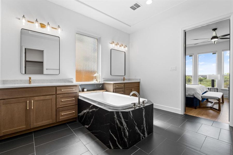 Ensuite bathroom featuring two vanities, a garden tub, plenty of natural light, dark tile patterned flooring, and recessed lighting Ensuite bathroom featuring two vanities, a garden tub, plenty of natural light, dark tile patterned flooring, and recessed lighting