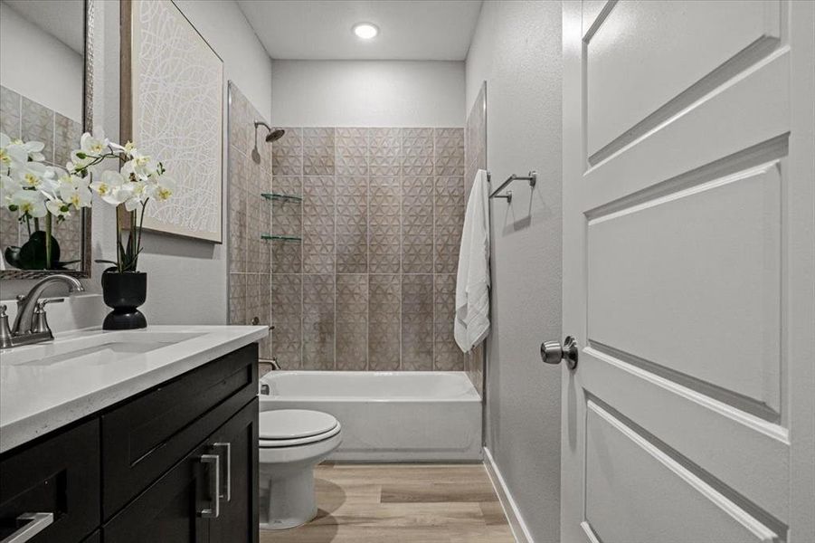 Full bathroom with vanity, tiled shower / bath combo, hardwood / wood-style flooring, and toilet