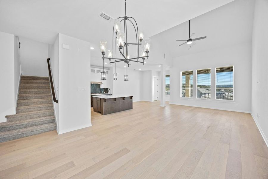 Unfurnished living room featuring a chandelier, light wood-type flooring, stairs, a ceiling fan, and high vaulted ceiling Unfurnished living room featuring a chandelier, light wood-type flooring, stairs, a ceiling fan, and high vaulted ceiling