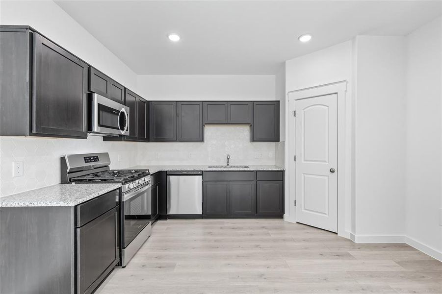 Kitchen with appliances with stainless steel finishes, backsplash, light wood-type flooring, recessed lighting, and light stone counters Kitchen with appliances with stainless steel finishes, backsplash, light wood-type flooring, recessed lighting, and light stone counters