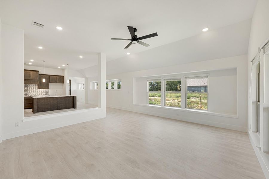 Open living area with light wood floors, ceiling fan, and open view into kitchen with dark cabinets