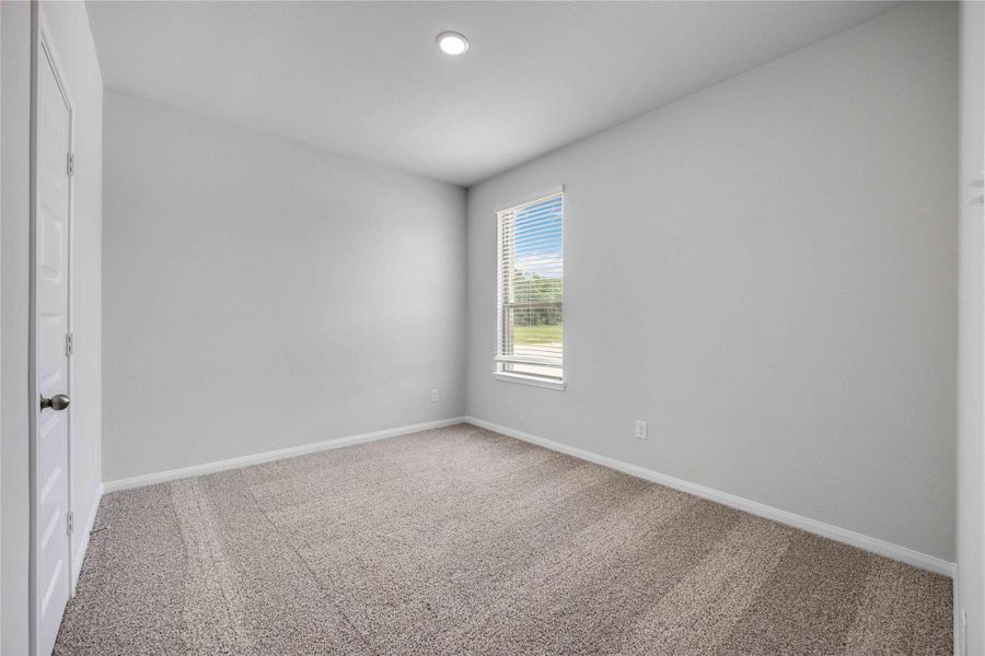 This cozy secondary bedroom features tall ceilings, recessed lighting and natural light from the window overlooking the acreage homesite.