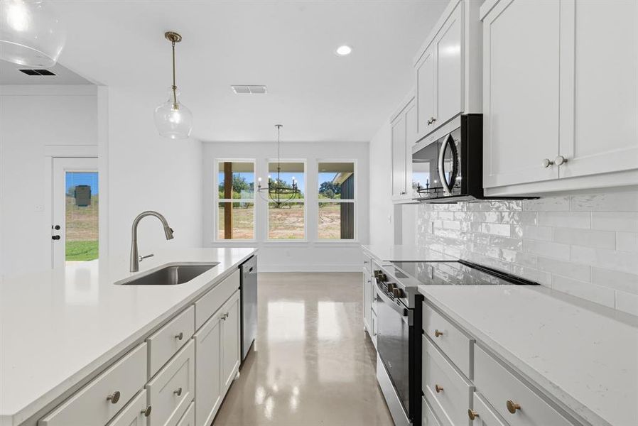 Kitchen featuring stainless steel appliances, white cabinetry, concrete flooring, decorative light fixtures, and backsplash