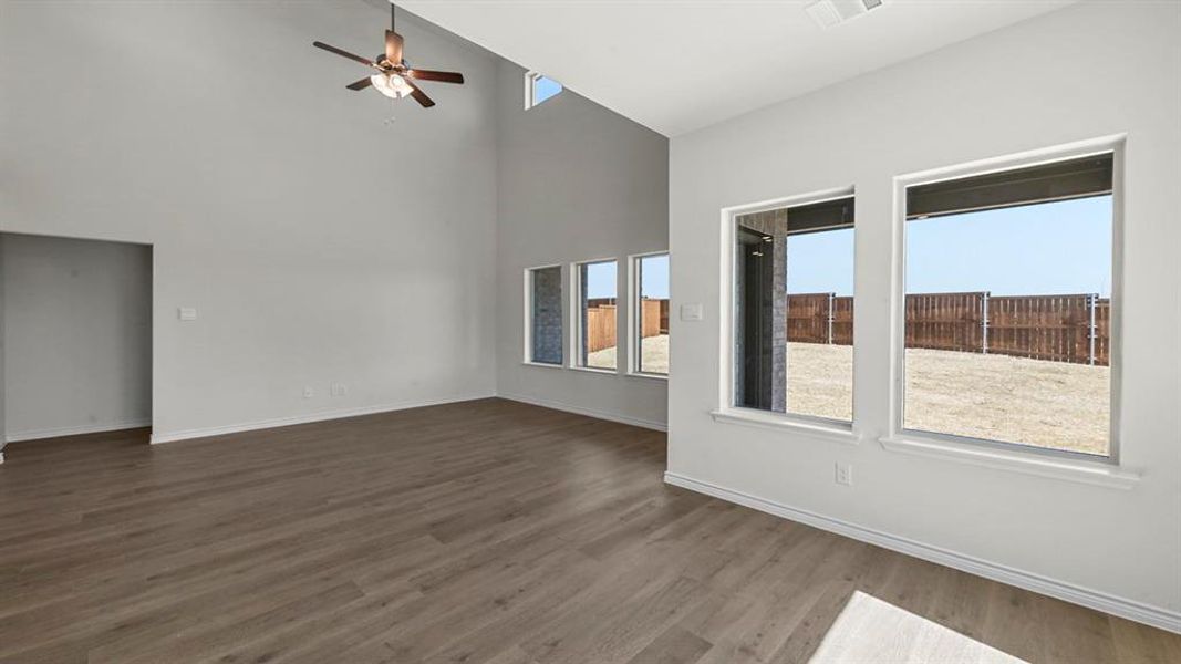 Empty room featuring dark wood-style flooring, ceiling fan, and a towering ceiling