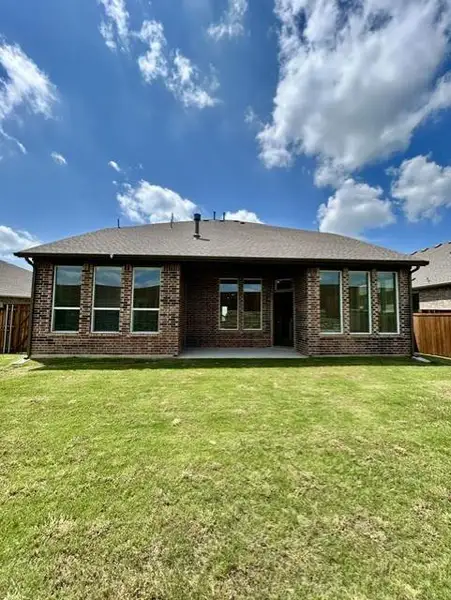 Expansive green lawn backing a brick exterior featuring multiple windows and a covered concrete patio Expansive green lawn backing a brick exterior featuring multiple windows and a covered concrete patio