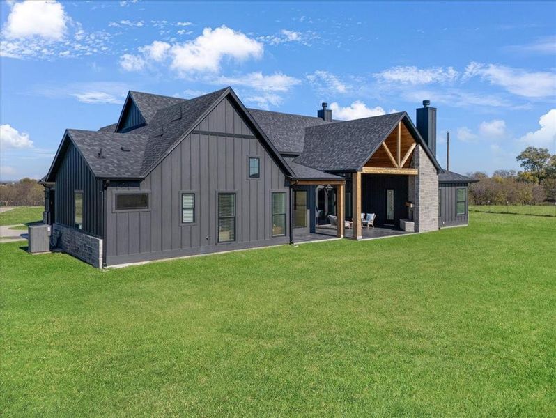 Back of property featuring a chimney, board and batten siding, a shingled roof, a patio, and a yard