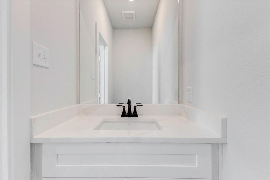 This sleek powder bath is perfectly placed for guests and everyday use. Features include a single quartz vanity with a matte black faucet, soft-close cabinetry, and a generously sized mirror for a streamlined, elegant look.