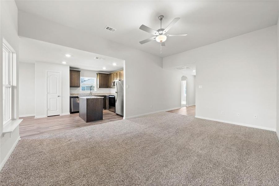 Unfurnished living room featuring ceiling fan, light carpet, arched walkways, baseboards, and recessed lighting