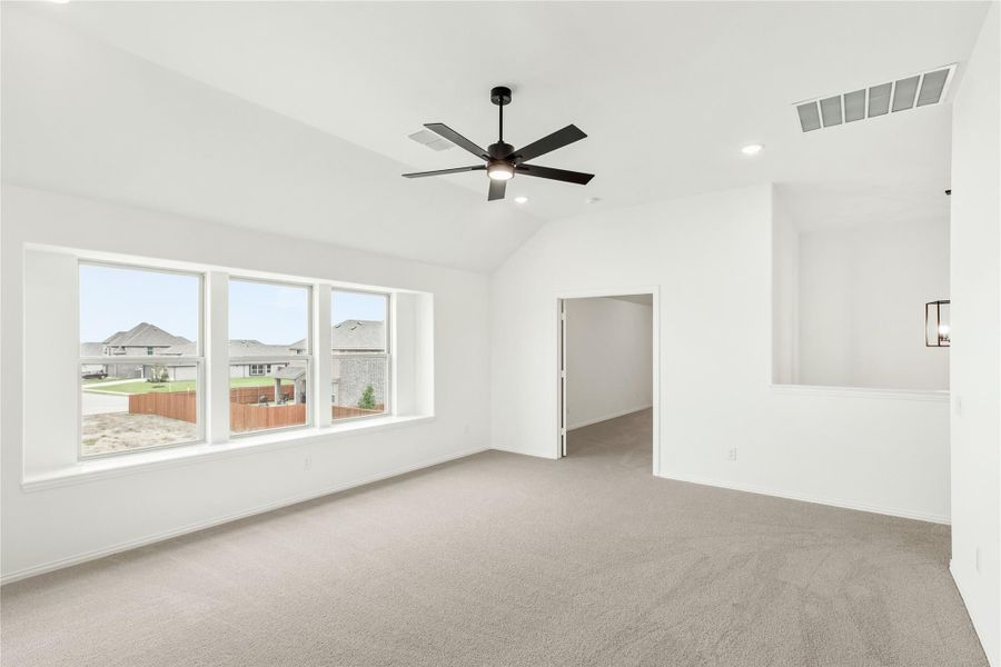 Empty bedroom with vaulted ceiling, ceiling fan, carpet flooring, and large windows overlooking neighborhood Empty bedroom with vaulted ceiling, ceiling fan, carpet flooring, and large windows overlooking neighborhood