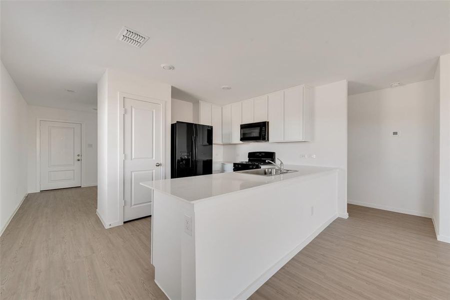 Kitchen featuring sink, light hardwood / wood-style flooring, kitchen peninsula, white cabinets, and black appliances