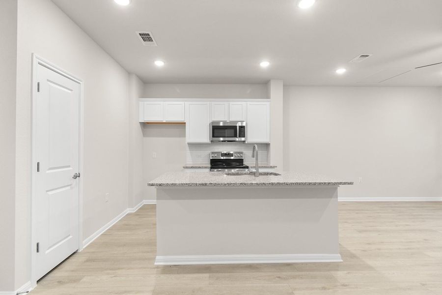 The kitchen features white cabinetry, stainless steel appliances, and a central island with a sink and granite-style countertop