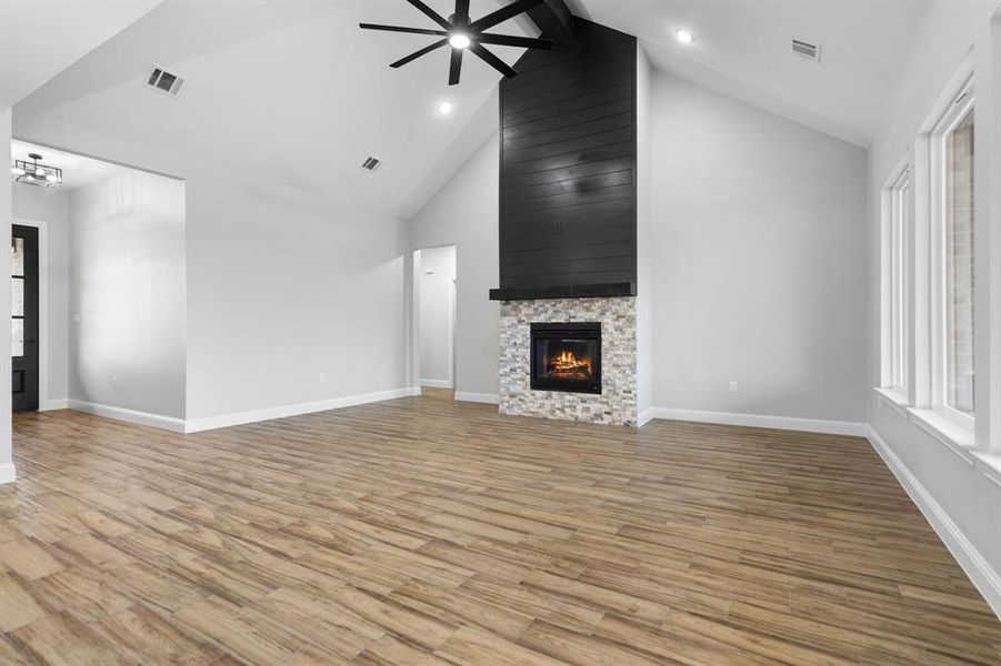 Unfurnished living room with a fireplace, ceiling fan with notable chandelier, high vaulted ceiling, and light hardwood / wood-style flooring