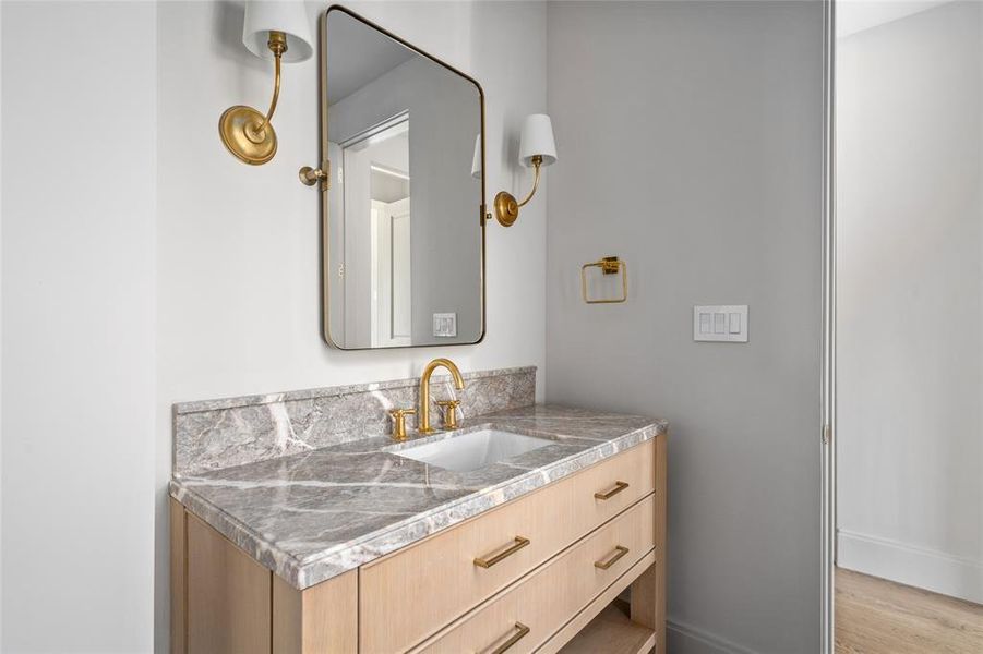 Refined and elegantly appointed, this ensuite bathroom features a stunning Taj Mahal marble vanity accented by designer Aerin sconces, which complement the sophisticated Caribbean Gray herringbone tile floors. Just out of frame, the glass-entry walk-in shower is a true statement piece, showcasing Flor de Pesco marble and a striking combination of Linea Moka and Sabbia Gloss subway tile walls. This luxurious space seamlessly blends modern design with timeless materials.