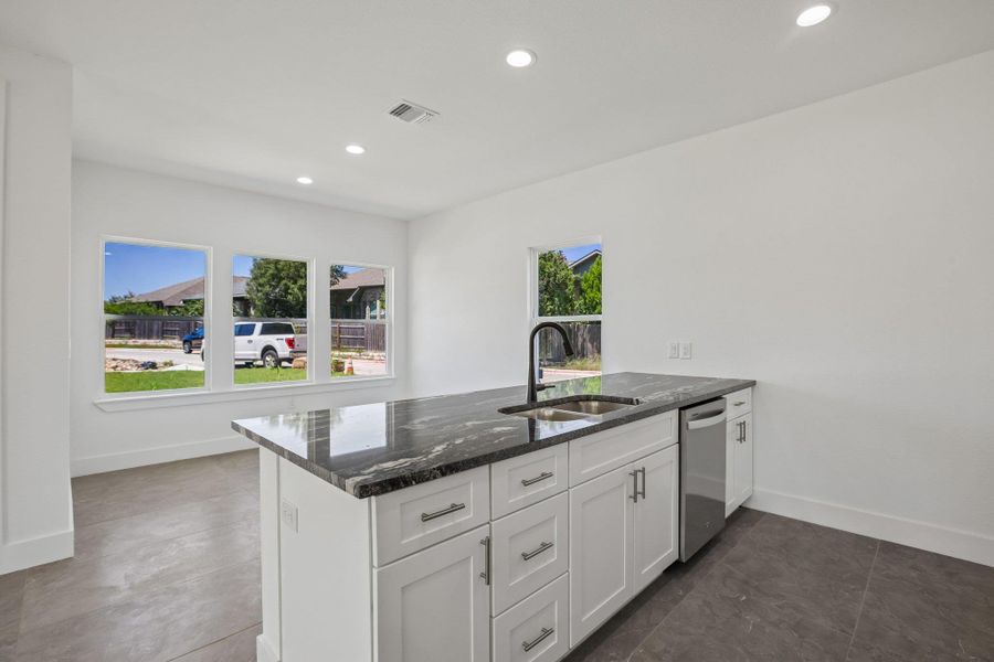 An open kitchen design features a dark stone island contrasting with modern tile floors.