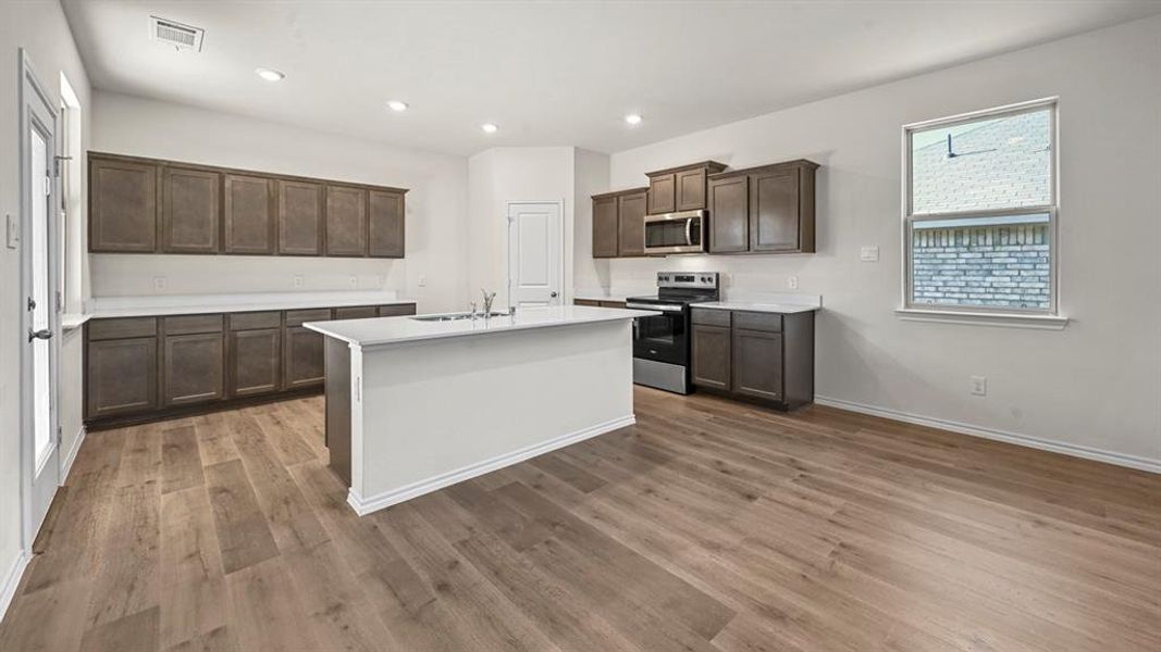Open-concept kitchen featuring an island, wood-finish flooring, dark wood cabinetry, stainless steel appliances, and white countertops