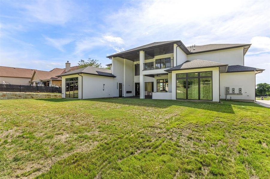 Rear exterior featuring a covered patio, upper-level balcony, and expansive glass panels