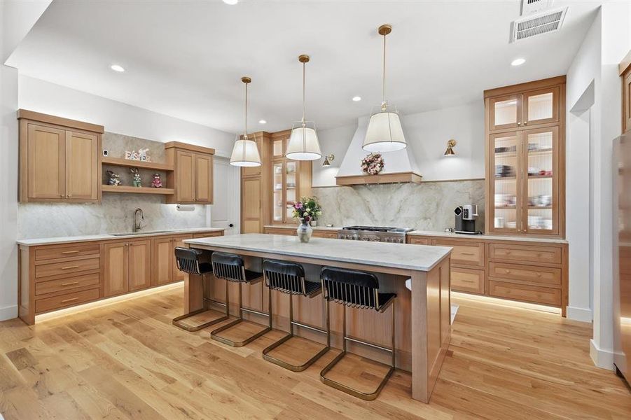 Kitchen with open shelves, a kitchen island, a kitchen bar, light wood-type flooring, and glass insert cabinets