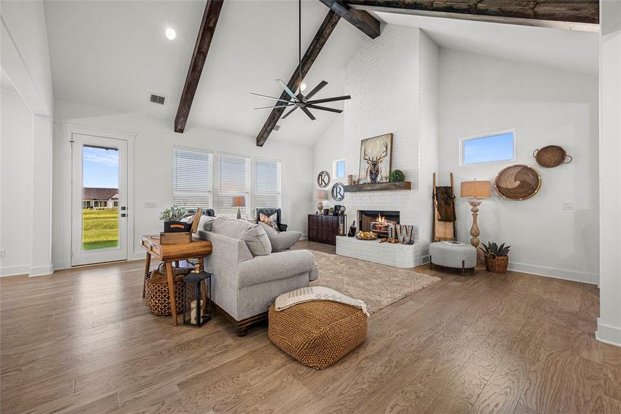 Living room featuring ceiling fan, beamed ceiling, a brick fireplace, hardwood / wood-style flooring, and high vaulted ceiling