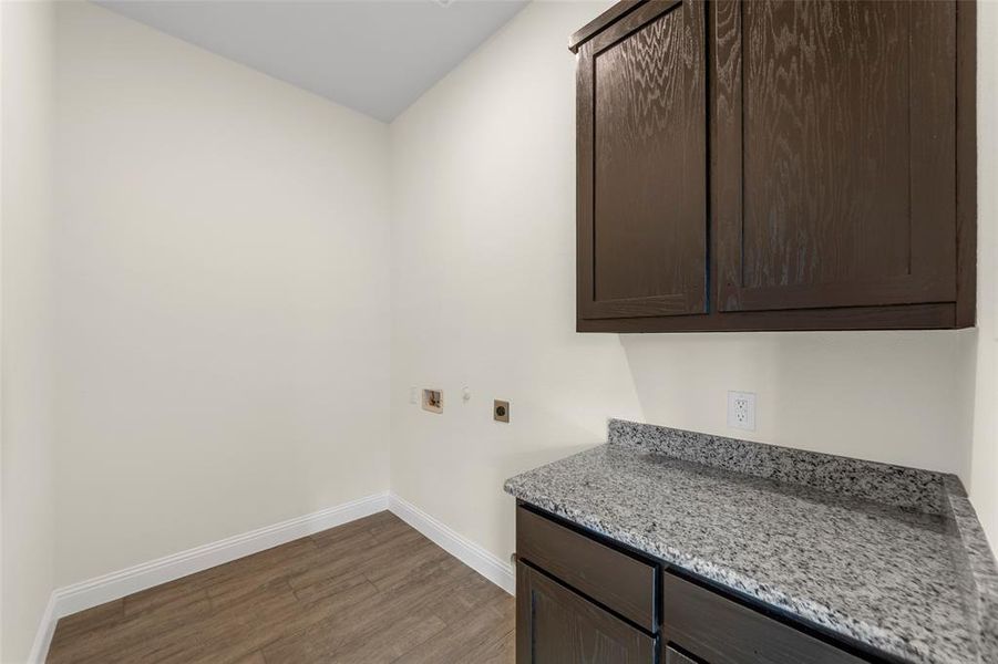 Utility area featuring dark wood-finish cabinetry, a speckled countertop, and wood-finish flooring