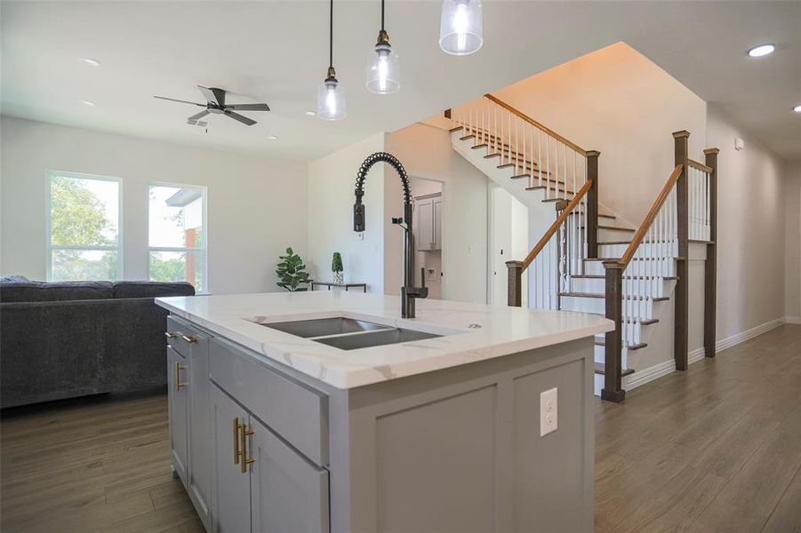 Kitchen with light stone counters, sink, decorative light fixtures, a kitchen island with sink, and dark hardwood / wood-style flooring