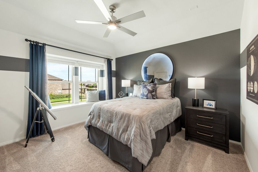 Bedroom with dark gray accent wall, ceiling fan, carpet, and large window with blue curtains