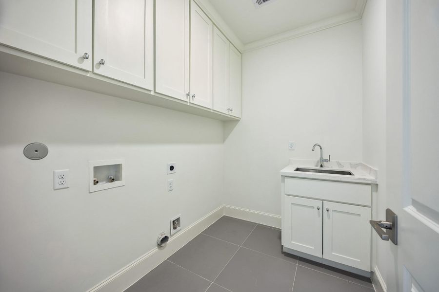 Dedicated laundry room with built-in cabinetry, sink and generous workspace.