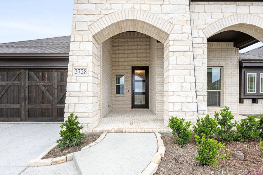 Stone and brick arched entryway with black front door, wood garage door, and landscaped walkway at home 2728 Stone and brick arched entryway with black front door, wood garage door, and landscaped walkway at home 2728