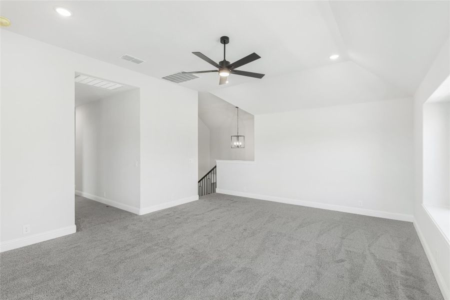 Spacious upstairs loft with gray carpet, vaulted ceiling, ceiling fan, and staircase opening Spacious upstairs loft with gray carpet, vaulted ceiling, ceiling fan, and staircase opening