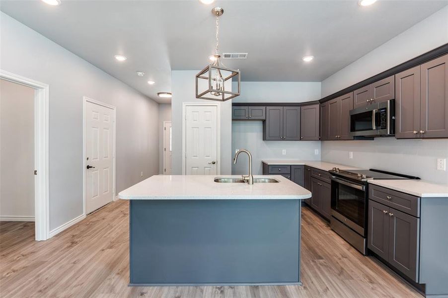 Kitchen featuring stainless steel appliances, sink, pendant lighting, light wood-type flooring, and an island with sink