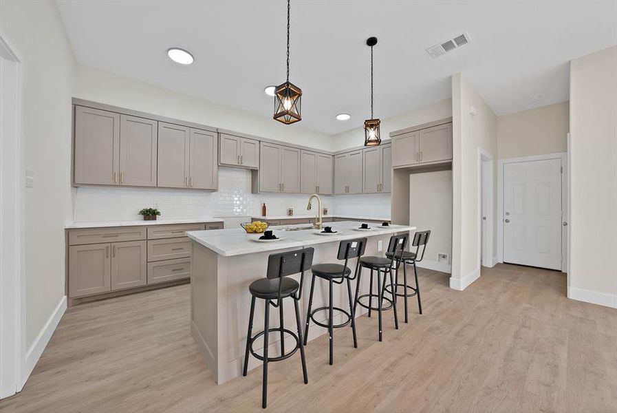 Kitchen featuring gray cabinetry, a kitchen bar, pendant lighting, a center island with sink, and light wood-style flooring