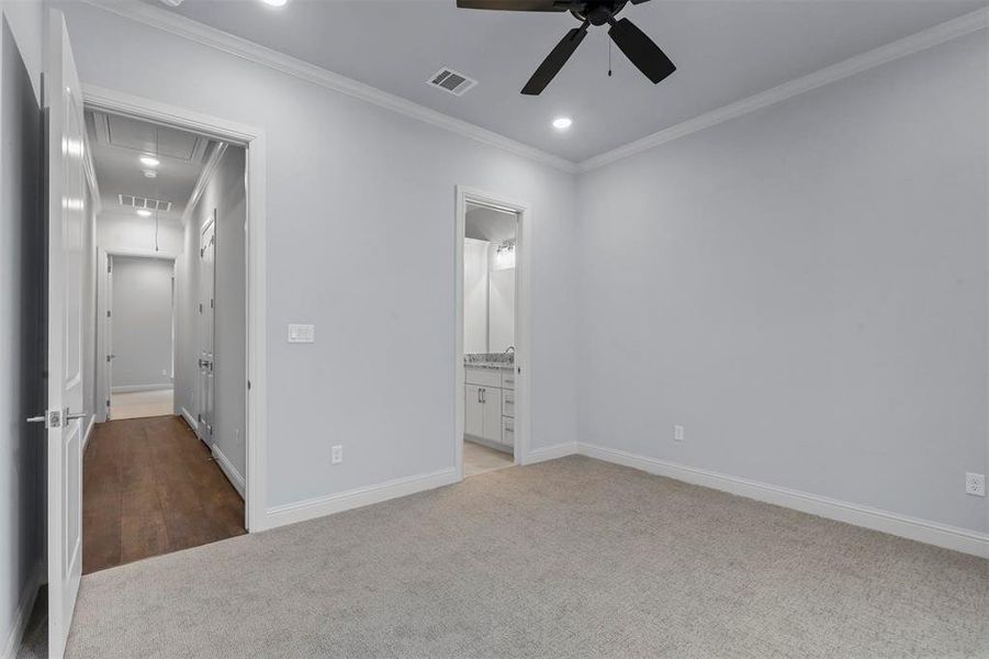 Unfurnished bedroom featuring ensuite bathroom, light carpet, ceiling fan, and crown molding