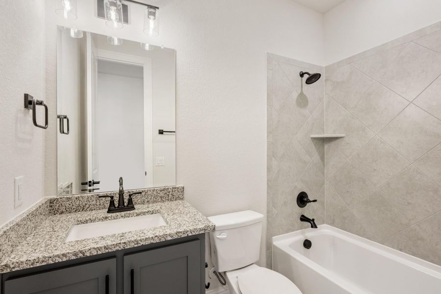 Bathroom with granite countertop vanity, tub-shower combo with diagonal tile surround, and dark bronze fixtures