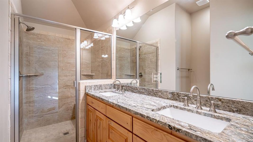Bathroom featuring double vanity, lofted ceiling, and a shower stall