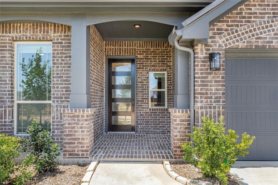 Brick home entrance with arched covered porch, modern glass-panel front door, and partial garage view