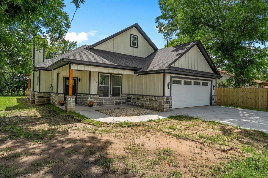 Contemporary facade featuring board and batten siding, stone veneer accents, an attached garage, a covered entry porch with a wood column, and a concrete driveway Contemporary facade featuring board and batten siding, stone veneer accents, an attached garage, a covered entry porch with a wood column, and a concrete driveway