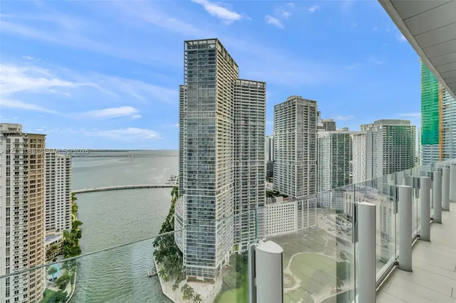 Private covered balcony with glass panel railing and tile flooring, showcasing an expansive cityscape and waterfront skyline Private covered balcony with glass panel railing and tile flooring, showcasing an expansive cityscape and waterfront skyline