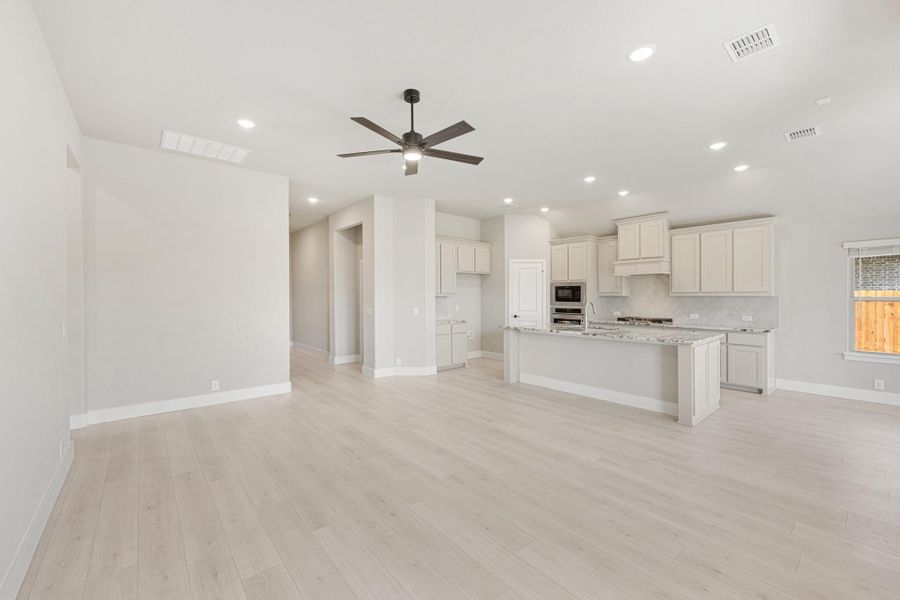 Open living area and kitchen with white cabinets, granite island, and light wood floors with ceiling fan