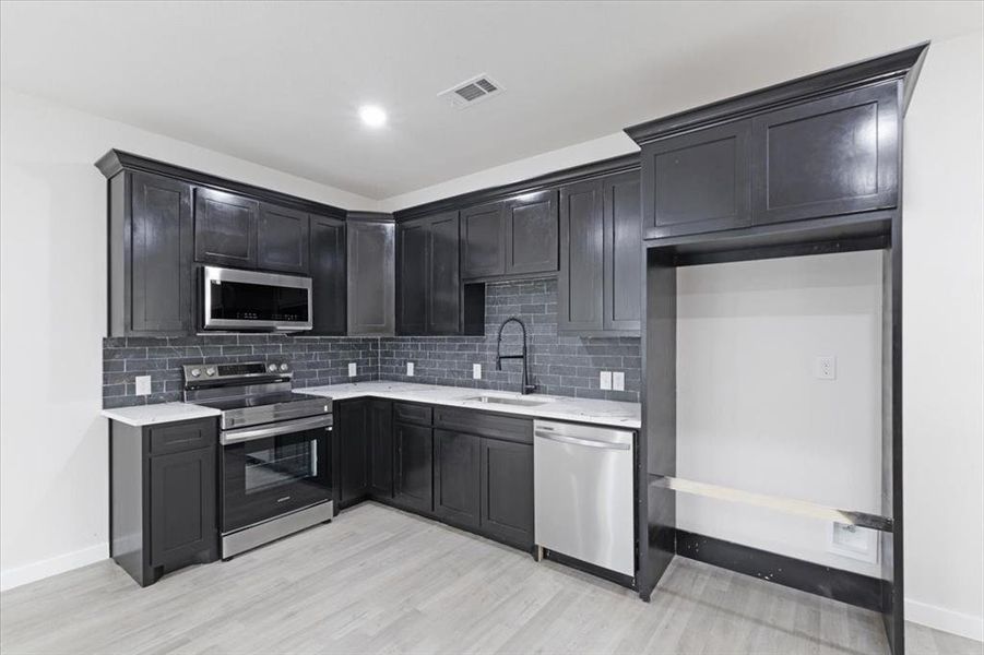 Kitchen with decorative backsplash, light wood-type flooring, sink, and appliances with stainless steel finishes