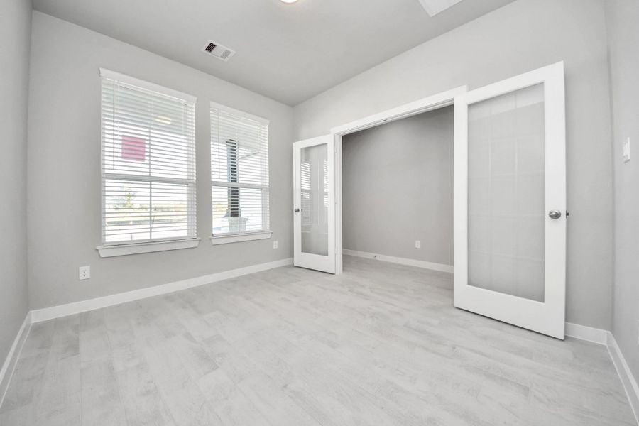Experience the perfect blend of sophistication and warmth in this home office, boasting elegant wood-look tile flooring and flooded with natural light from expansive windows and French doors. Sample photo of completed home with similar floor plan. Actual colors and selections may vary.